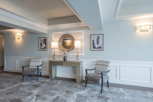 sitting room with crown molding, wainscoting, dark carpet, and a decorative wall