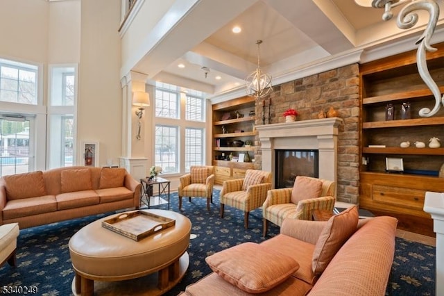 living room featuring built in shelves, a glass covered fireplace, a high ceiling, and an inviting chandelier