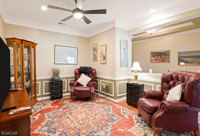 living area featuring visible vents, a wainscoted wall, crown molding, light wood-style floors, and a decorative wall