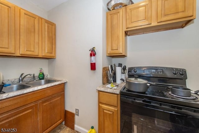 kitchen featuring light countertops, black range with electric cooktop, a sink, and baseboards