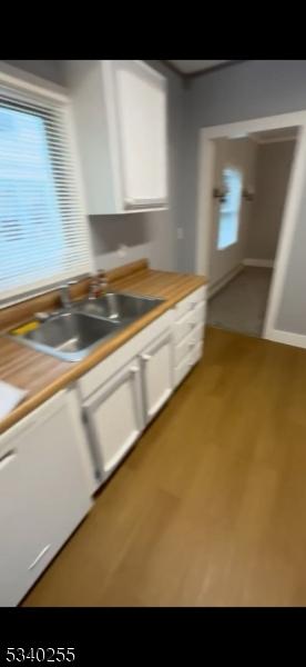 kitchen with light countertops, white cabinetry, a sink, wood finished floors, and dishwasher