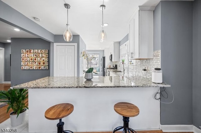 kitchen with a sink, decorative backsplash, light stone countertops, and a peninsula