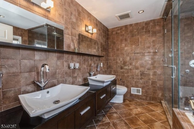 bathroom featuring a stall shower, a sink, visible vents, and tile walls