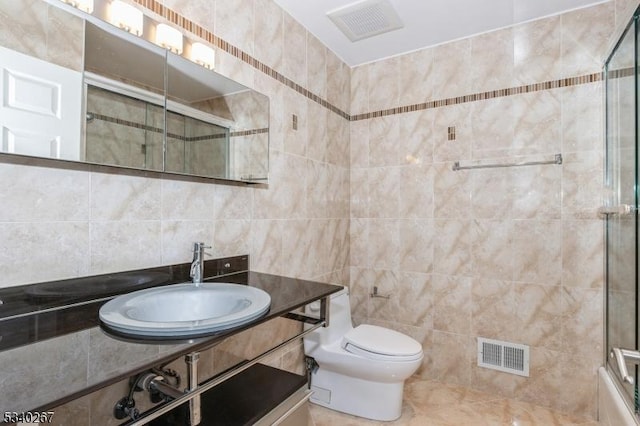 full bath featuring toilet, a sink, visible vents, tile walls, and a tile shower