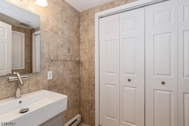 bathroom with a sink, visible vents, tile walls, a closet, and baseboard heating