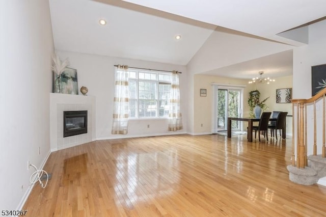 unfurnished living room featuring a tiled fireplace, lofted ceiling, stairway, light wood-style floors, and a chandelier