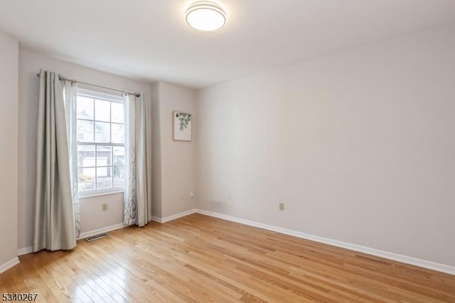 empty room with light wood-style floors, visible vents, and baseboards