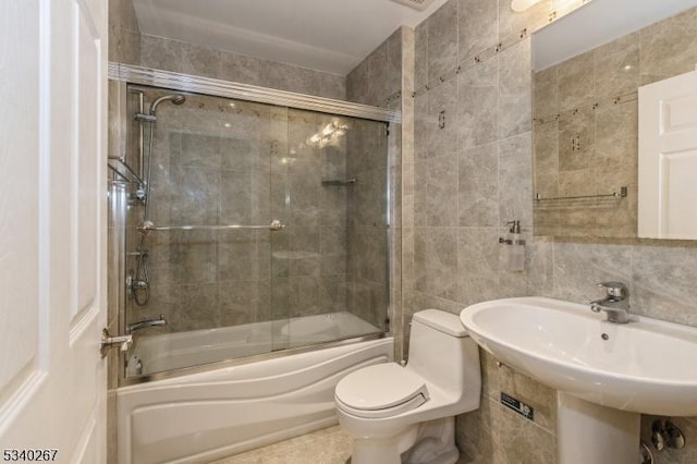 bathroom featuring toilet, combined bath / shower with glass door, a sink, and tile walls