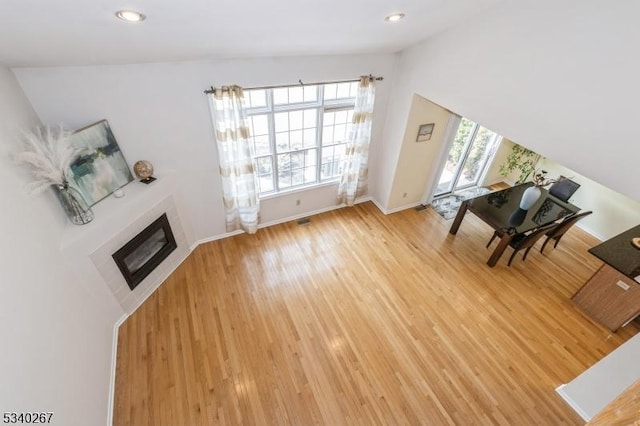 unfurnished living room with light wood finished floors, plenty of natural light, a tile fireplace, and baseboards