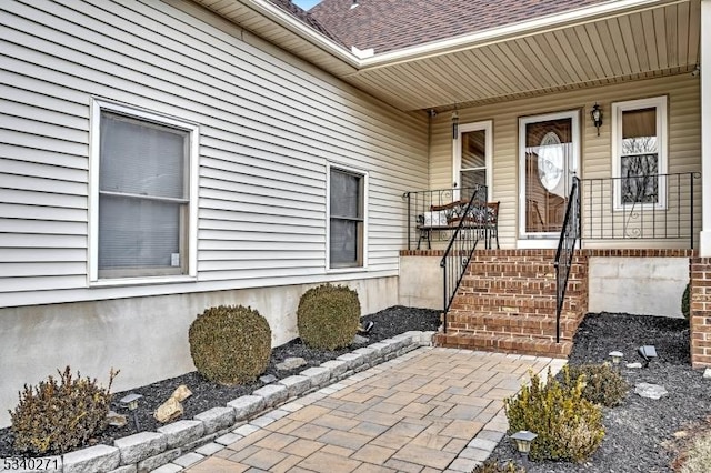 entrance to property with a shingled roof and a porch