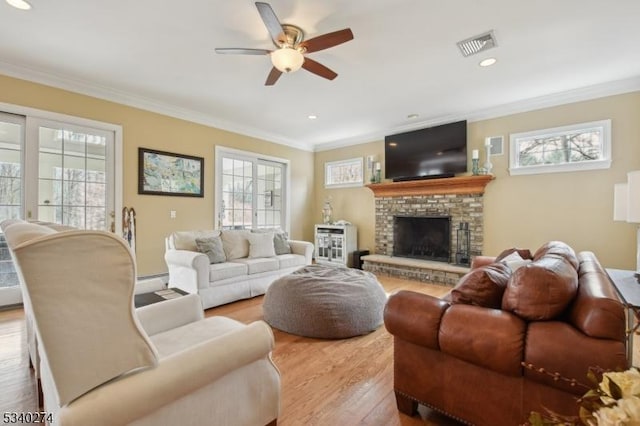 living room with visible vents, ceiling fan, ornamental molding, a fireplace, and wood finished floors