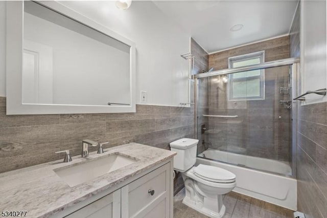 full bath with enclosed tub / shower combo, toilet, a wainscoted wall, vanity, and tile walls