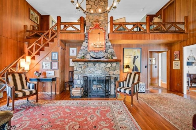 living area featuring a fireplace, an inviting chandelier, wooden walls, wood finished floors, and stairs