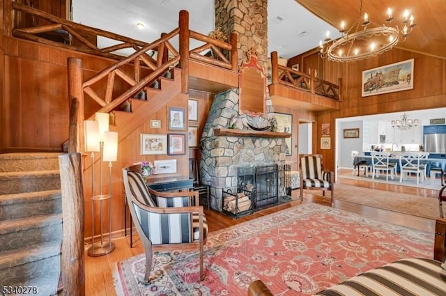 living room featuring wooden walls, a fireplace, wood finished floors, stairway, and an inviting chandelier