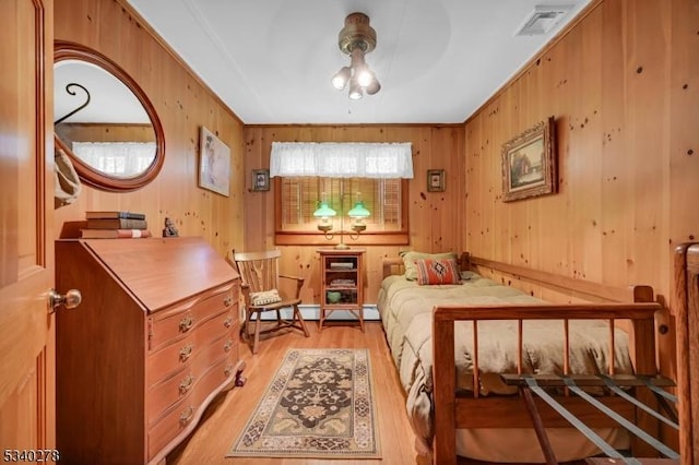 bedroom featuring light wood finished floors, visible vents, a baseboard heating unit, and wood walls