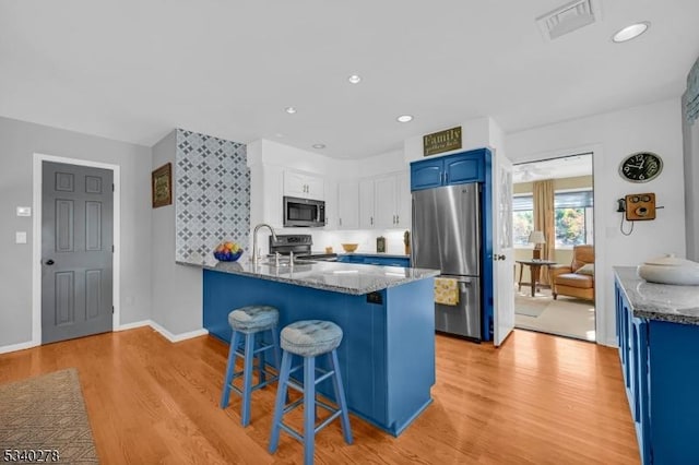 kitchen with a peninsula, appliances with stainless steel finishes, dark stone countertops, and blue cabinetry