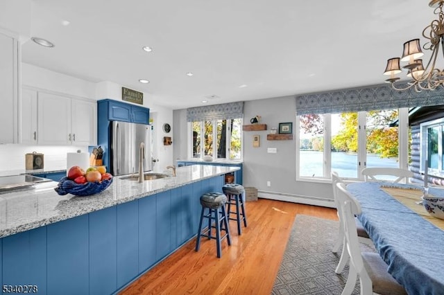 kitchen featuring a sink, blue cabinetry, baseboard heating, freestanding refrigerator, and light stone countertops