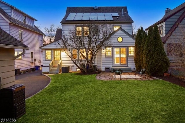 back of house featuring entry steps, a patio, central AC unit, a yard, and roof mounted solar panels