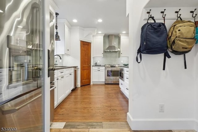 kitchen featuring decorative backsplash, appliances with stainless steel finishes, a sink, wall chimney range hood, and wood finished floors