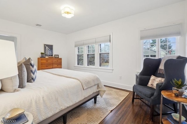 bedroom with multiple windows, visible vents, baseboards, and wood finished floors