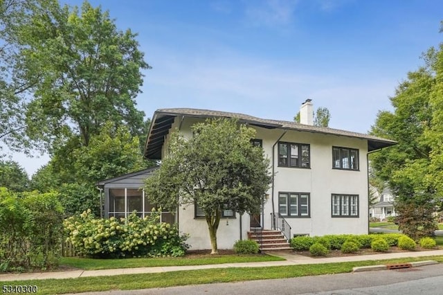 view of front facade featuring a chimney, a sunroom, and stucco siding