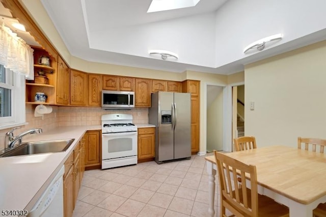 kitchen with a sink, appliances with stainless steel finishes, a skylight, light countertops, and decorative backsplash