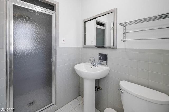 bathroom with tile patterned floors, a wainscoted wall, toilet, tile walls, and a shower stall