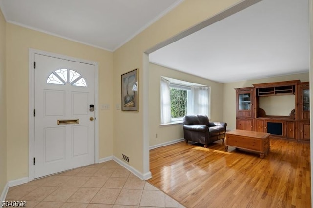 entrance foyer featuring light tile patterned flooring, baseboards, visible vents, and ornamental molding