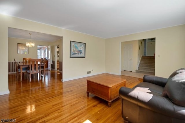 living area with stairway, baseboards, light wood finished floors, and a chandelier