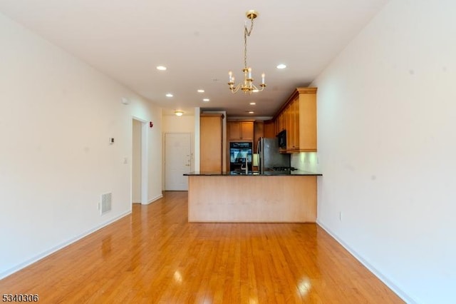 kitchen featuring visible vents, black appliances, light wood finished floors, dark countertops, and pendant lighting