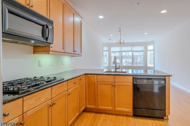 kitchen featuring a peninsula, black appliances, light wood-style flooring, and a sink