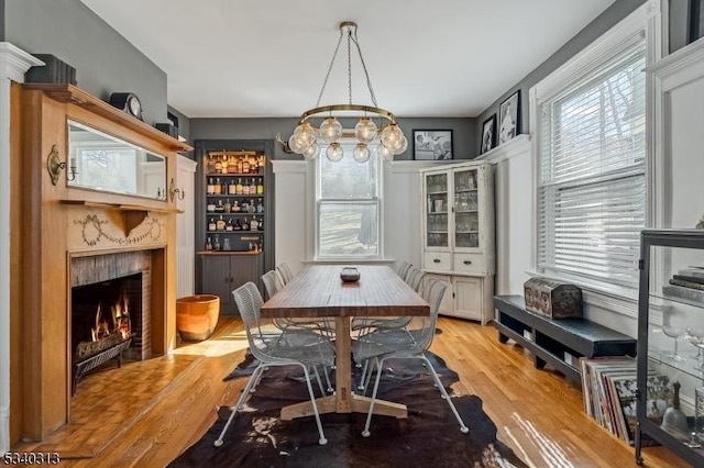 dining room with light wood-type flooring, a warm lit fireplace, and a chandelier