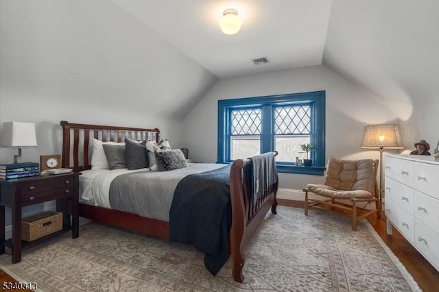 bedroom with visible vents, lofted ceiling, baseboards, and light wood-style flooring