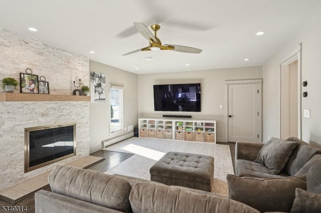 living room featuring recessed lighting, a baseboard heating unit, ceiling fan, a stone fireplace, and wood finished floors