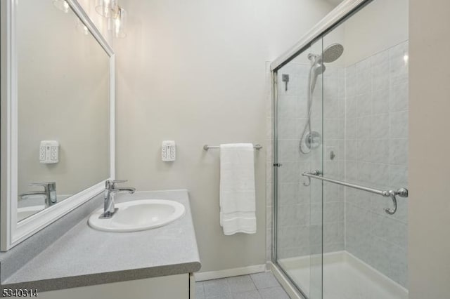 full bathroom featuring a stall shower, tile patterned flooring, vanity, and baseboards