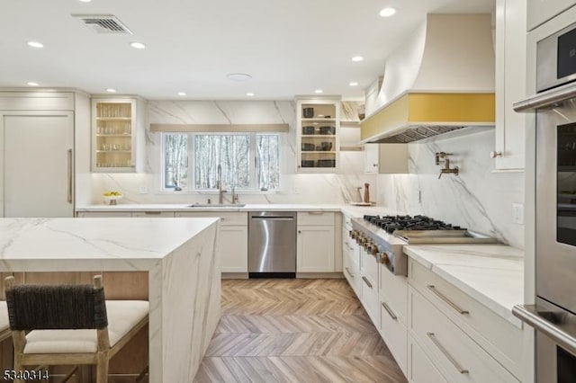 kitchen with visible vents, glass insert cabinets, stainless steel appliances, premium range hood, and a sink