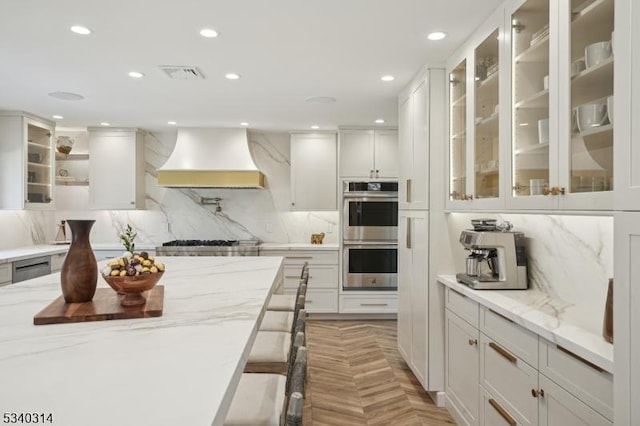 kitchen featuring glass insert cabinets, custom exhaust hood, white cabinets, and light stone counters