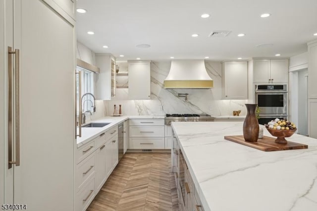 kitchen with white cabinets, appliances with stainless steel finishes, light stone countertops, glass insert cabinets, and custom range hood