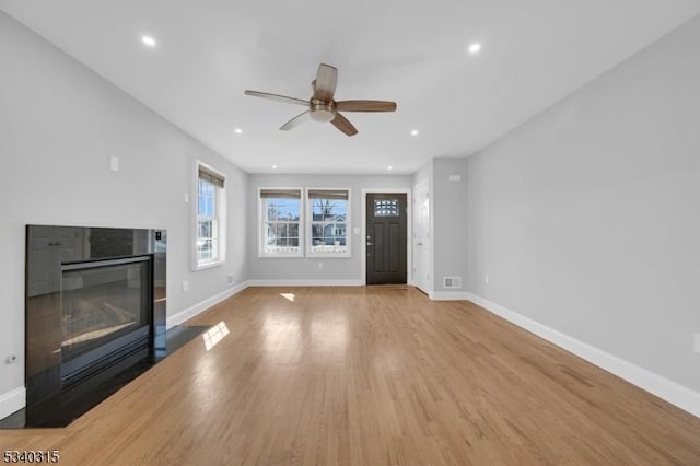 unfurnished living room featuring light wood-style floors, a glass covered fireplace, and baseboards