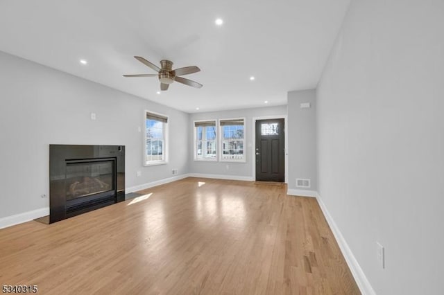 unfurnished living room featuring light wood-style floors, a fireplace with flush hearth, visible vents, and baseboards