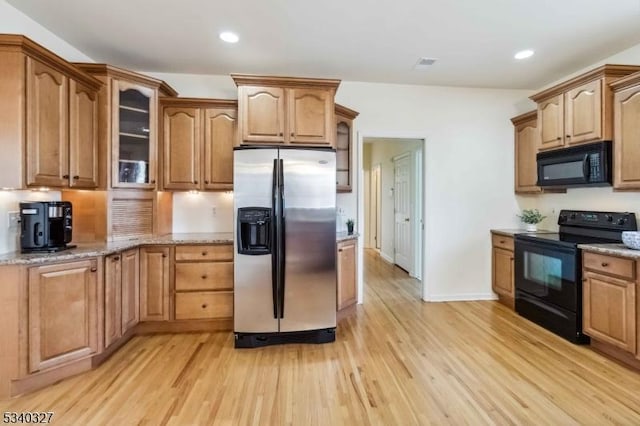 kitchen featuring glass insert cabinets, light stone countertops, light wood-type flooring, black appliances, and recessed lighting