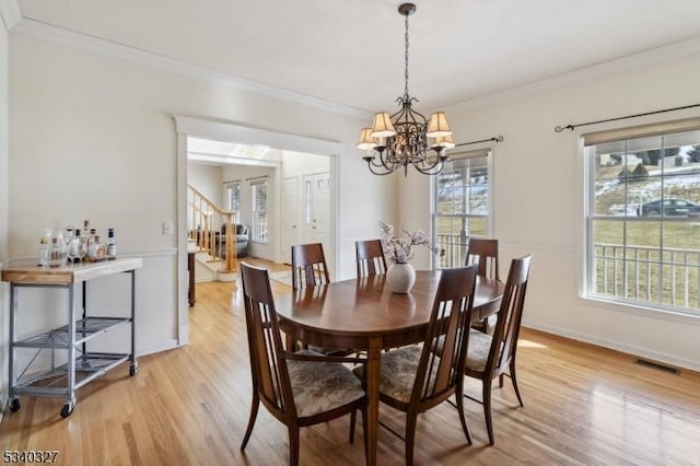 dining space featuring crown molding, light wood finished floors, visible vents, stairway, and an inviting chandelier