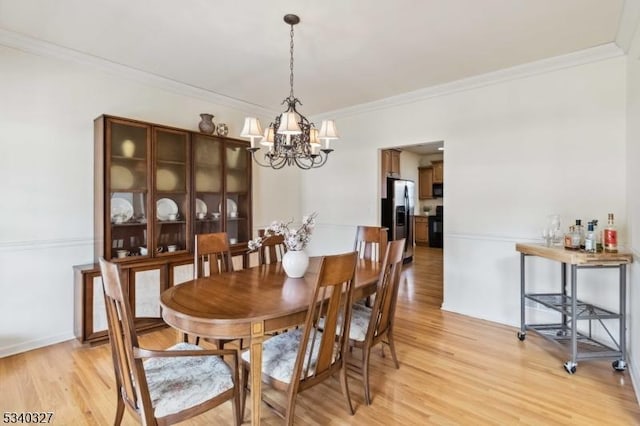 dining area featuring baseboards, crown molding, light wood finished floors, and an inviting chandelier