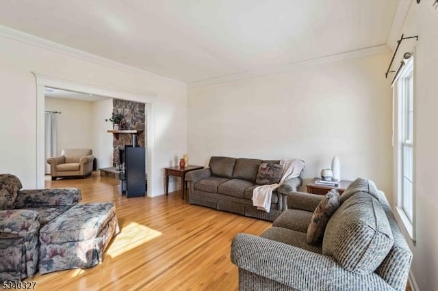 living area with ornamental molding, wood finished floors, and a stone fireplace