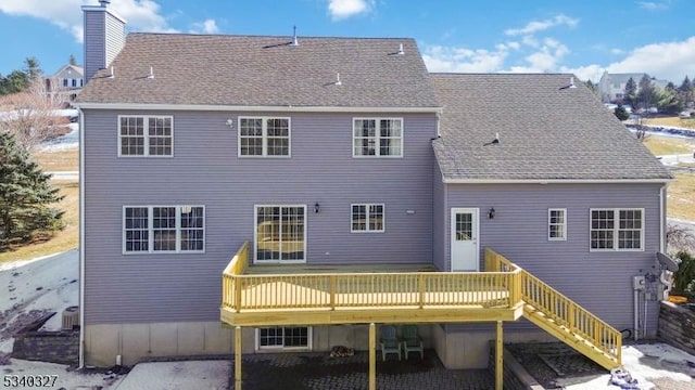 rear view of property featuring a shingled roof, a chimney, a wooden deck, and stairs