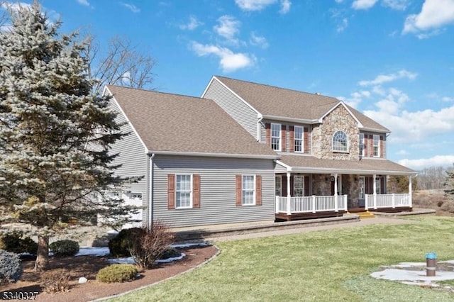 view of front of house with stone siding, a shingled roof, a front lawn, and covered porch