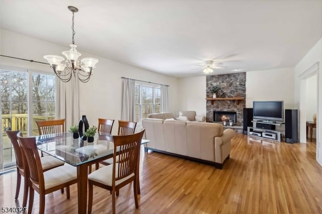 dining area featuring light wood-style flooring, a fireplace, and ceiling fan with notable chandelier