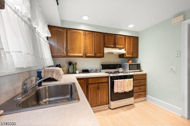 kitchen with white gas stove, under cabinet range hood, a sink, light countertops, and stainless steel microwave