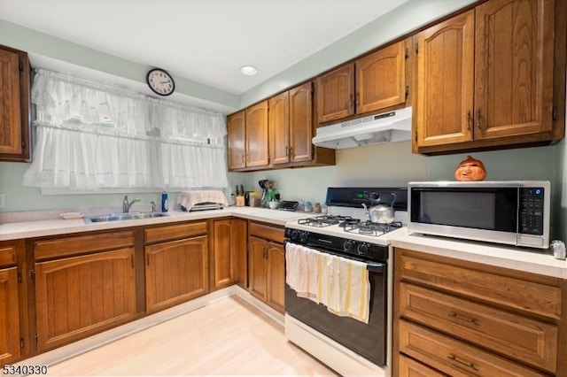 kitchen featuring light countertops, stainless steel microwave, gas stove, a sink, and under cabinet range hood