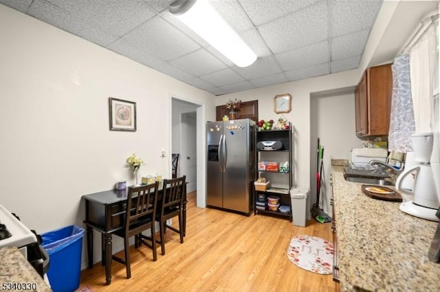 kitchen with light wood finished floors, a paneled ceiling, brown cabinetry, a sink, and stainless steel fridge with ice dispenser